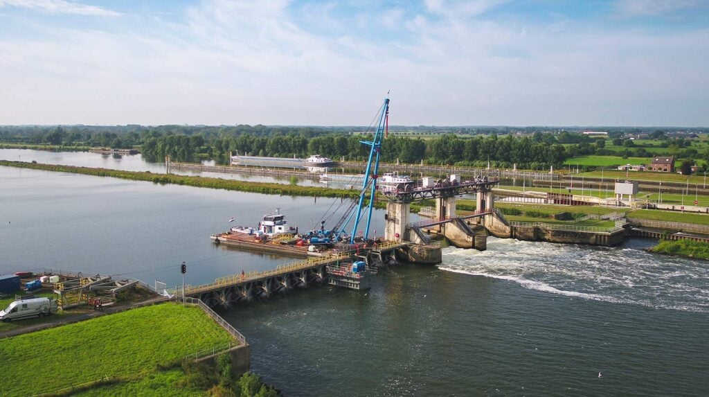 Luchtfoto van een stuw in een rivier met kraanschip en werkploeg bij onderhoudswerkzaamheden.