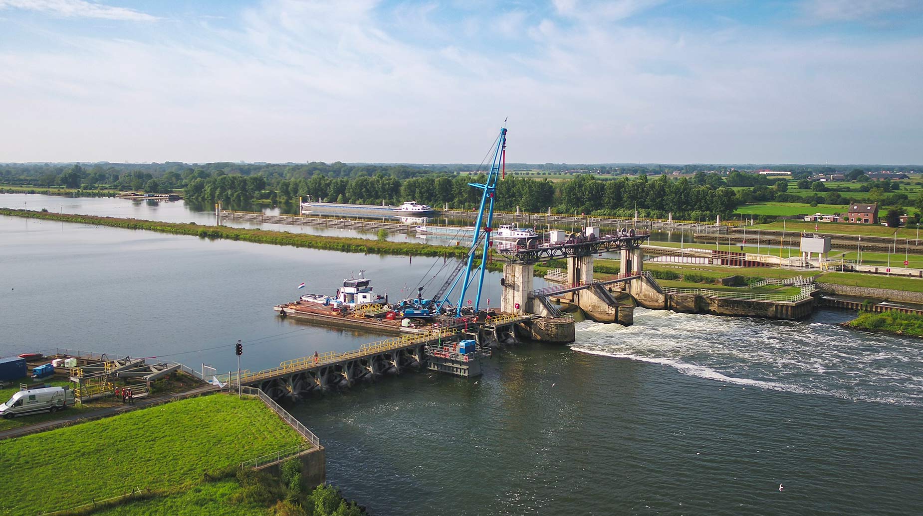 Luchtfoto van een stuw in een rivier met kraanschip en werkploeg bij onderhoudswerkzaamheden.