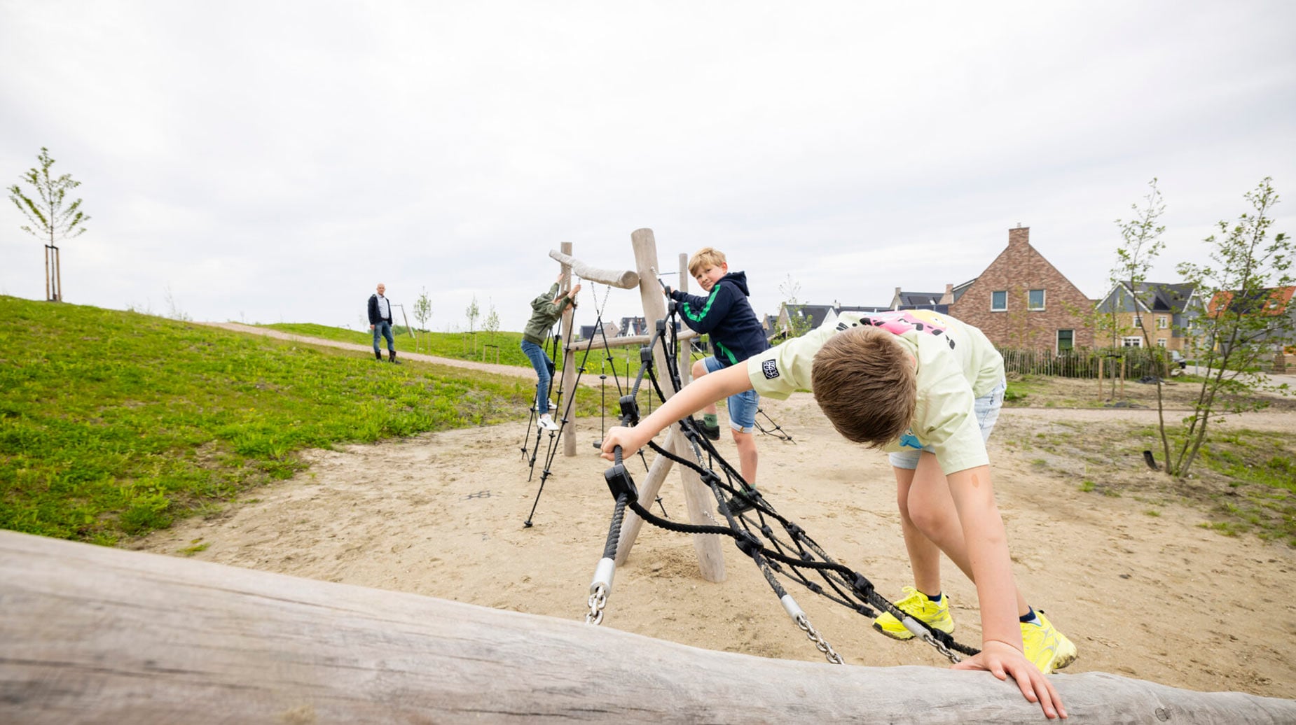 Kinderen klimmen op een houten klimtoestel met touwen op een speelplek in een nieuwbouwwijk.