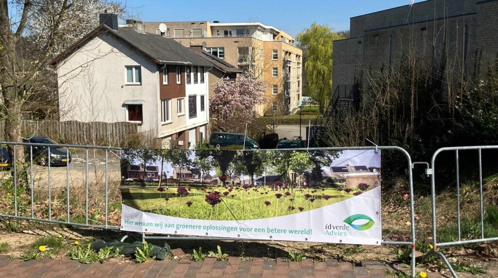 Bouwhek met idverde Advies-banner over herinrichting van een braakliggend terrein in een woonwijk.