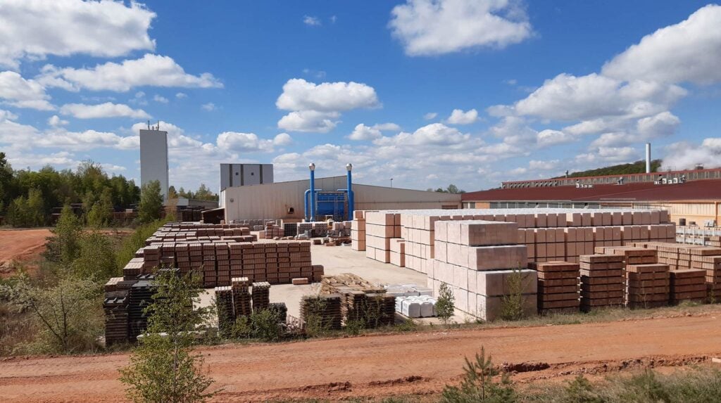 Buitenopslag van bakstenen en betonblokken bij een steenfabriek, omgeven door onbeplante grond.
