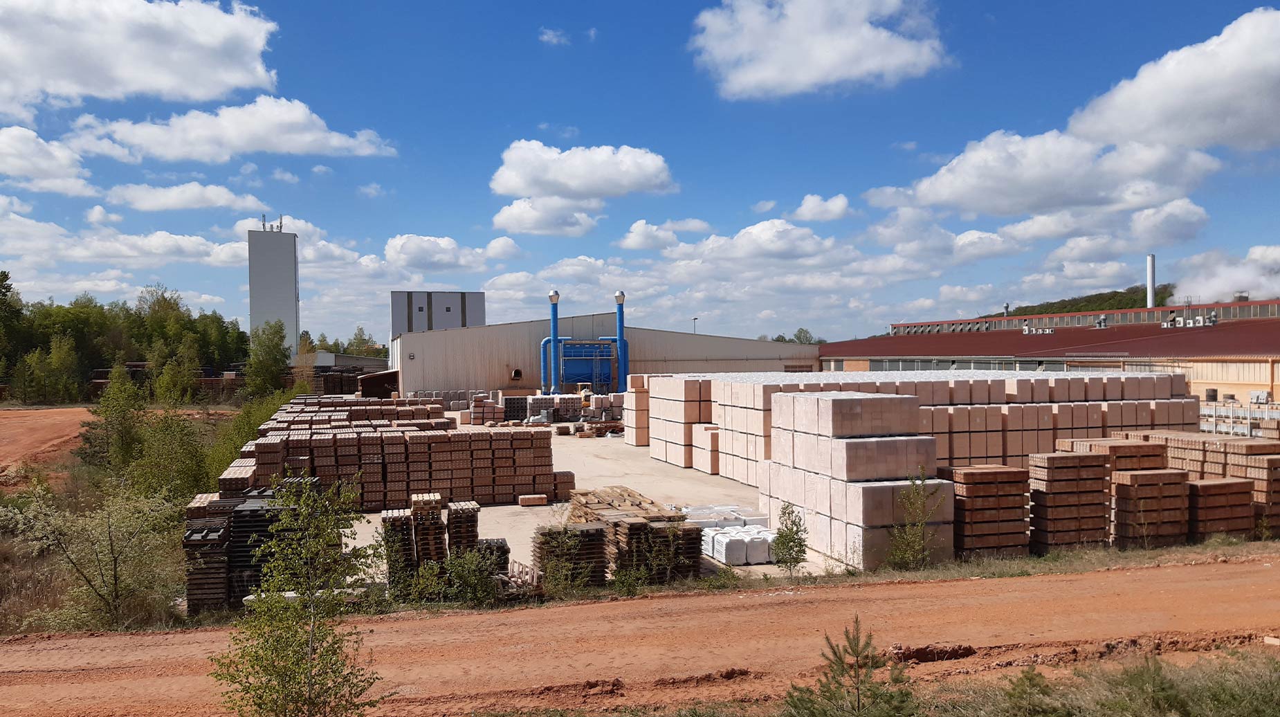 Buitenopslag van bakstenen en betonblokken bij een steenfabriek, omgeven door onbeplante grond.