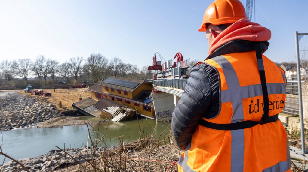 Medewerker van idverde kijkt uit over een rivier naar een verzakte woonboot bij een brug in aanbouw.