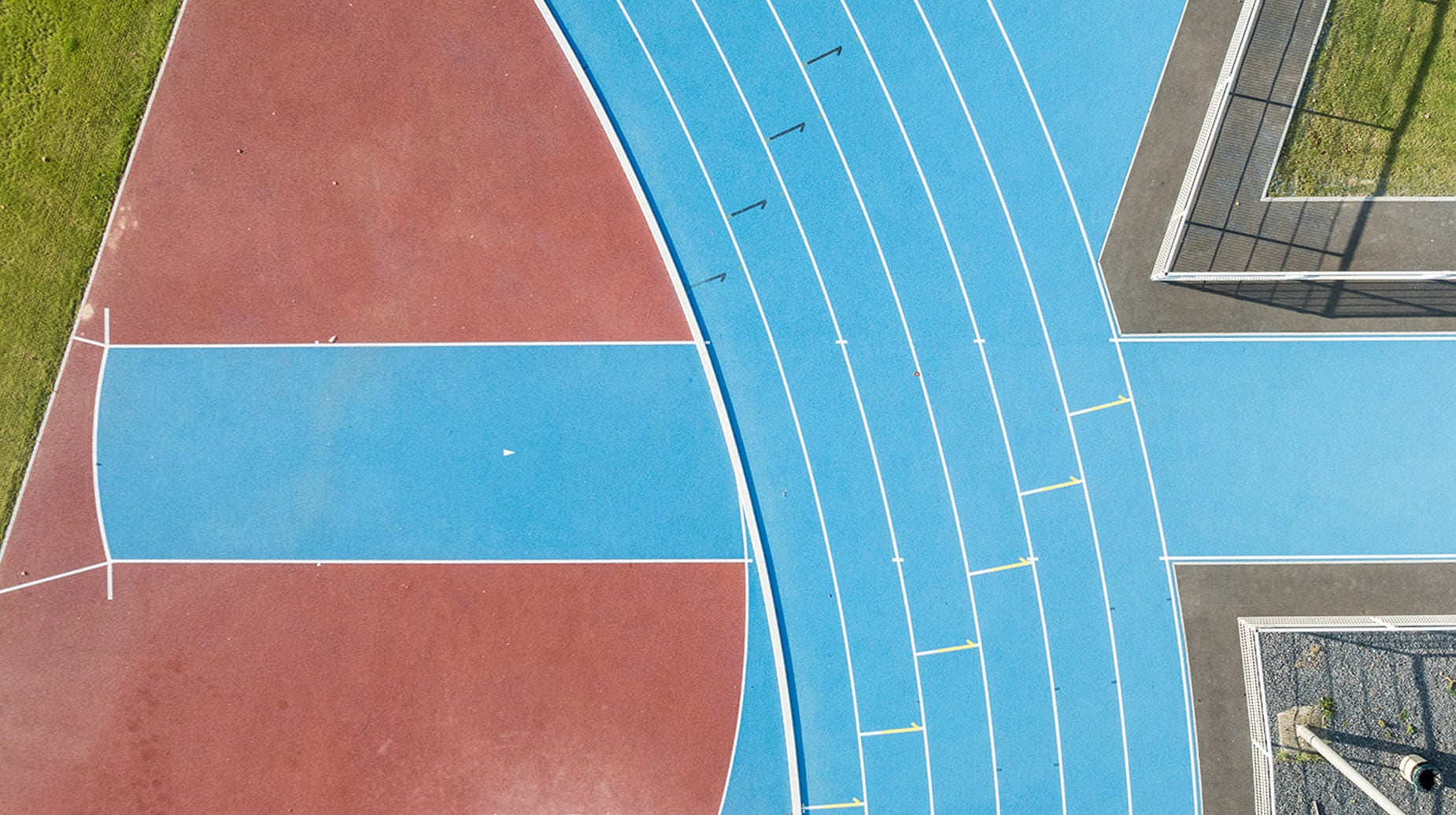 Luchtfoto van een blauwe atletiekbaan met rood sportveld naast een voetbaldoel.