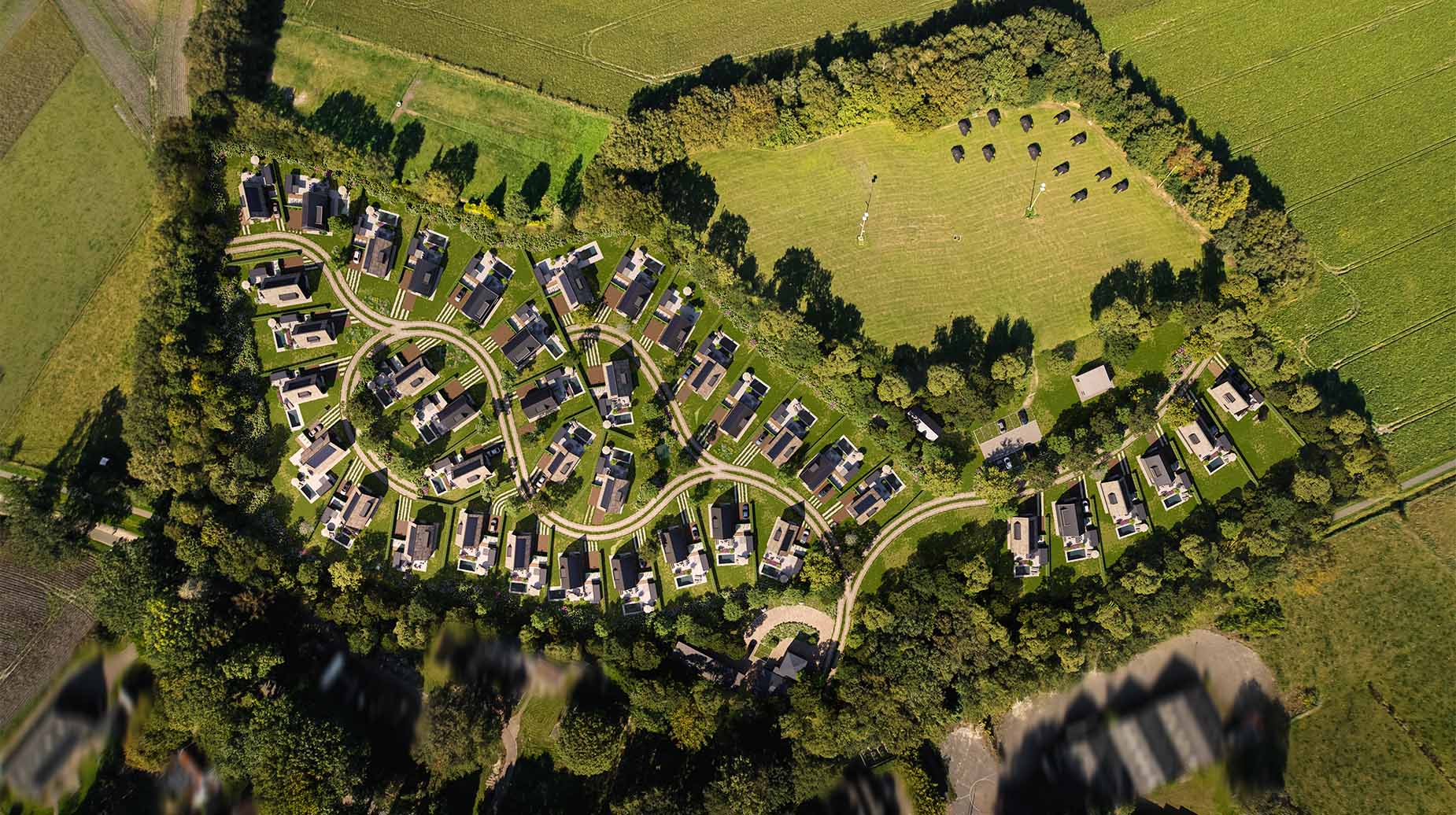 Luchtfoto van vakantiepark met bungalows in groene omgeving, omzoomd door bomen en akkers.