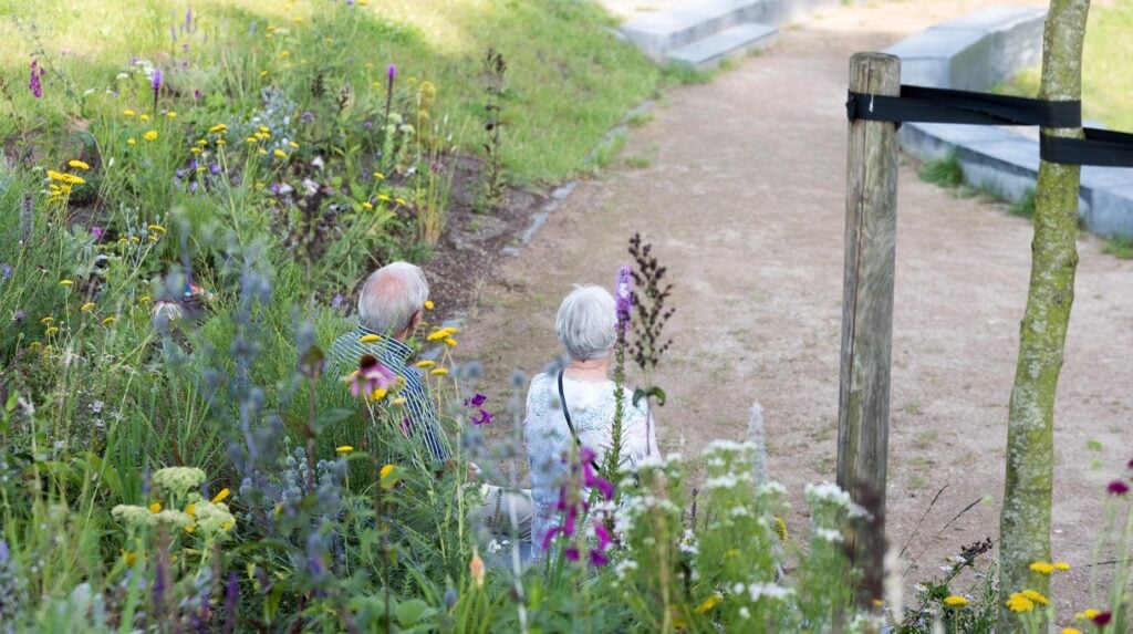 Twee ouderen wandelen langs een bloemrijke border met vaste planten naast een grindpad.