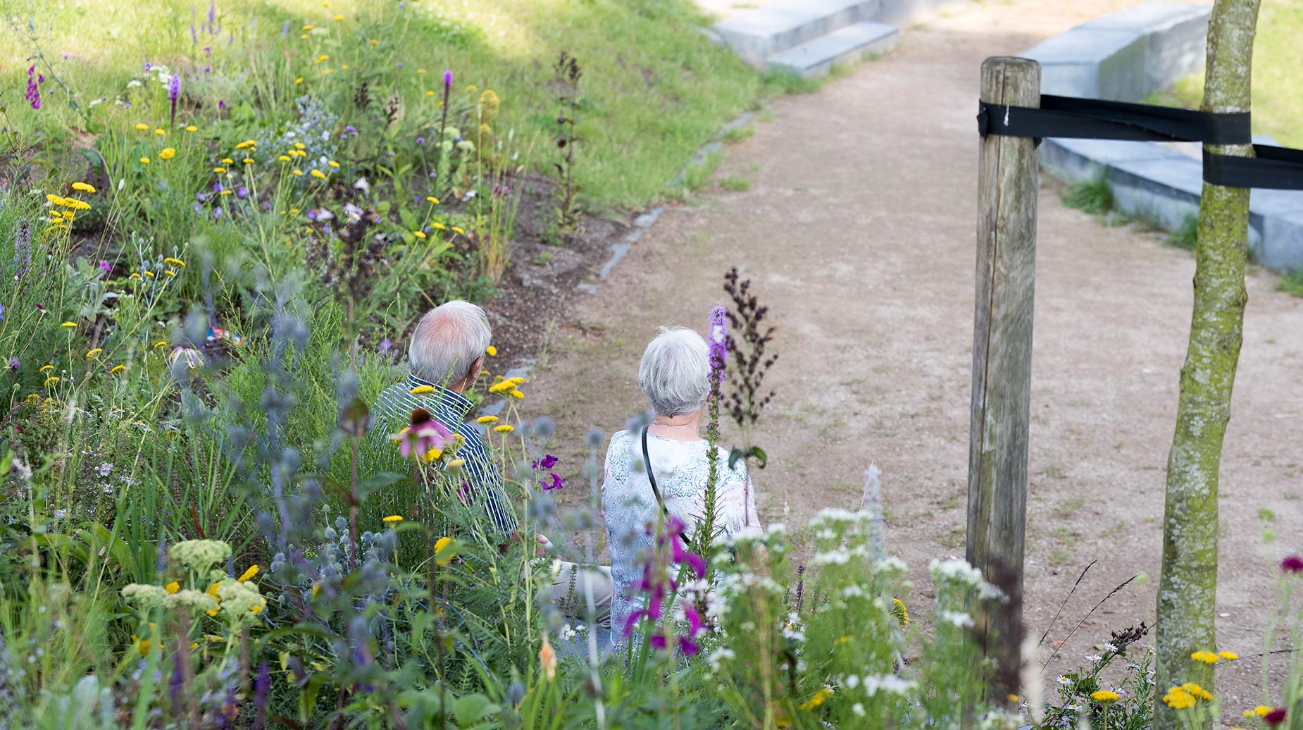 Twee bezoekers lopen over een grindpad langs een bloemrijke border met vaste planten.