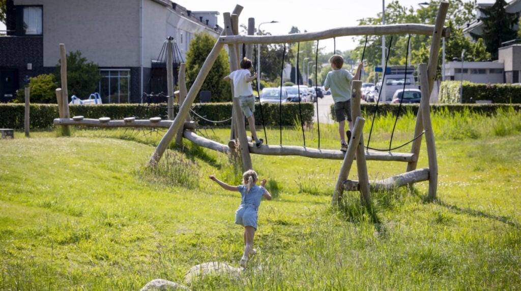Kinderen spelen op een houten klimtoestel in een groene woonwijk.