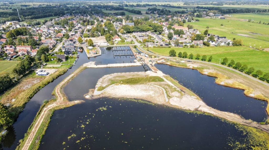 Luchtfoto van een dorp met jachthaven en nieuw aangelegde waterpartijen met zandeilanden.