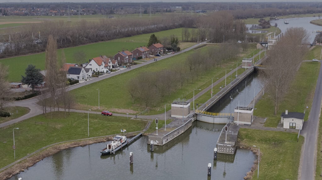 Luchtfoto van een sluis in een Nederlands waterwegenlandschap met woonhuizen en groene weilanden