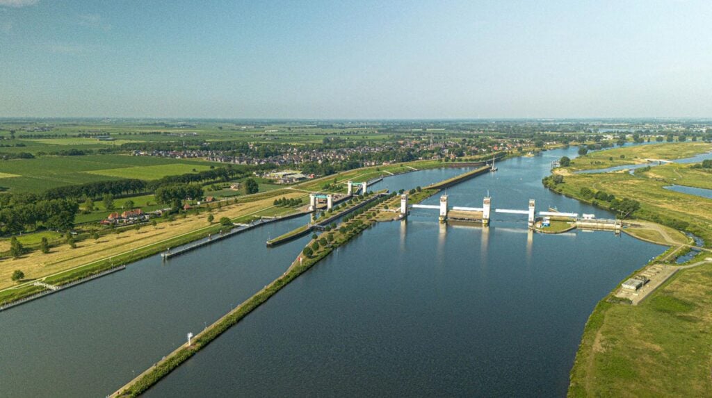 Luchtfoto van sluiscomplex en groene oevers langs de Maas met omliggend polderlandschap.