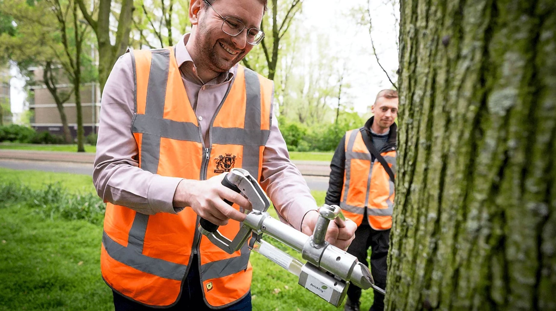 Medewerker van idverde injecteert een iep met een vaccin via een metalen injectiepistool, collega kijkt toe.