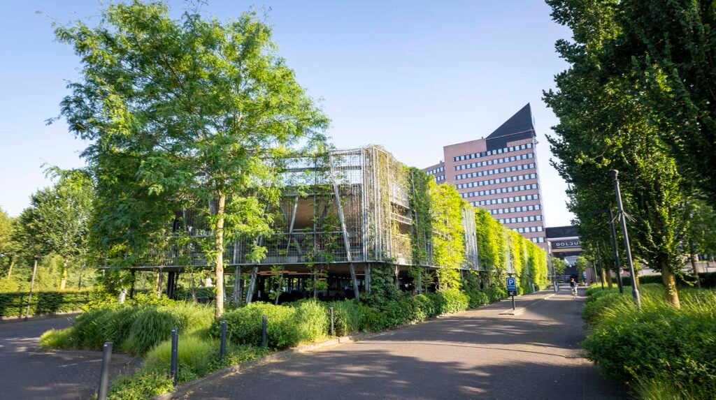 Groen bedrijventerrein met begroeide parkeergarage en kantoorgebouw omgeven door bomen en struiken