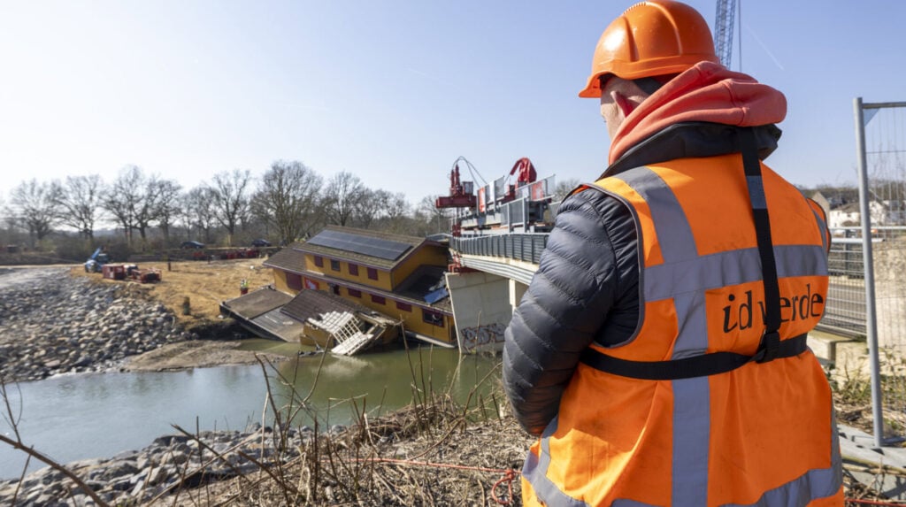 Medewerker van idverde in veiligheidskleding houdt toezicht bij werkzaamheden aan de oever van de Maas nabij een gedeeltelijk ingestort pand bij de Stuwweg in Maastricht.