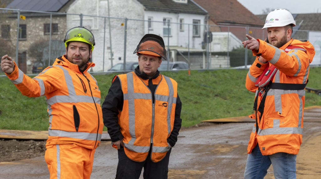 Drie idverde-medewerkers in oranje veiligheidskleding overleggen op een bouwplaats in Maastricht