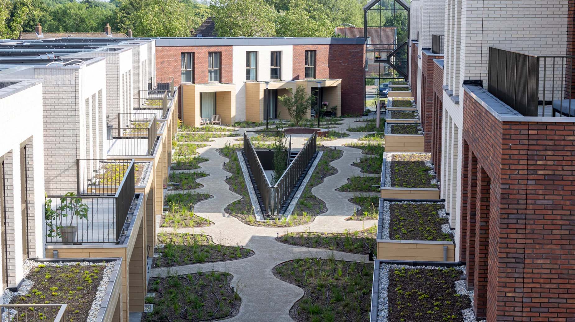 Luchtaanzicht van een groene binnenplaats tussen nieuwbouwwoningen met golvende paden en sedumdaken