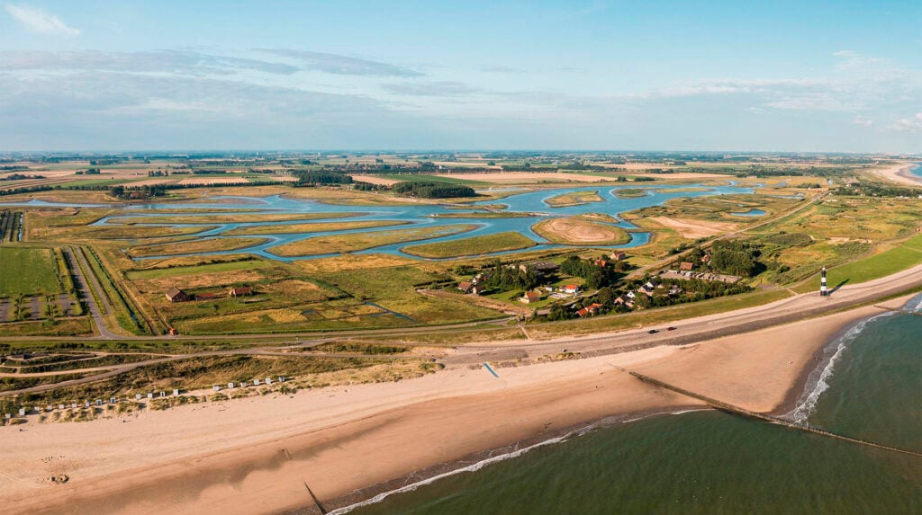 Luchtfoto van kustlandschap met kreken, duinen en strand bij een vuurtoren.