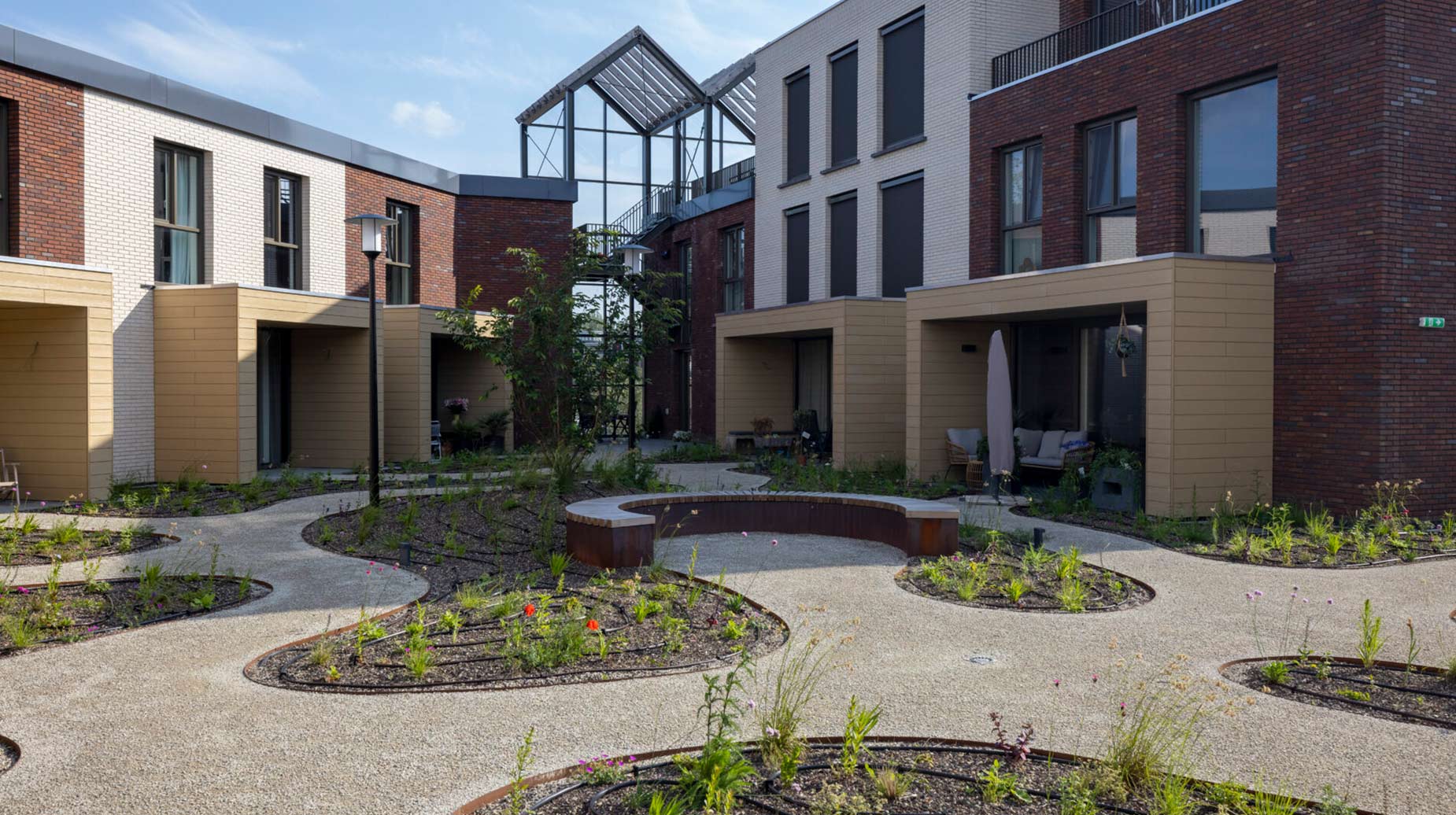 Binnentuin met organisch gevormde plantvakken, grindpaden en gebogen zitbank tussen woningen aan de Wervenkade in Dordrecht.